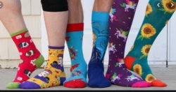 three pairs of legs wearing mismatched socks with colorful patterns